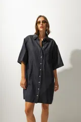 Vestido corto de denim azul, corte camisero holgado, mangas cortas amplias, cuello clásico, cierre frontal con botones, bolsillo aplicado en el pecho y pequeño bordado lateral en el dobladillo.