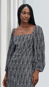Vestido corto negro con estampado de lunares blancos, escote cuadrado, mangas largas abullonadas y corte evasé.