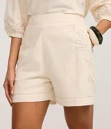 Short de cintura alta color crema, con bolsillos laterales y bordados abstractos en los costados.