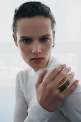 Anillo de diseño geométrico en tono dorado con una pieza rectangular de piedra ojo de tigre incrustada en el centro.