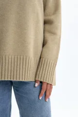 Polera de punto en color verde, con cuello alto, mangas largas con puños acanalados y aberturas laterales en el ruedo.