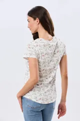 Remera de manga corta con cuello redondo, confeccionada en algodón con estampa de diseño floral en tonos rosados y verdes sobre base beige.