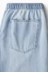 Pantalón de denim celeste de corte holgado, con cintura elástica ajustable con cordón, bolsillos delanteros y traseros, y pierna ancha.