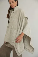 Capa de lana fina con cuello alto, cierre frontal con botones ocultos y bolsillos plaqué. Presenta aberturas laterales versátiles que permiten usarla como poncho o ruana, con terminaciones envivadas.