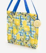 Bolsa plegable con estampa de limones y patrón de cuadros azules y blancos. Cuenta con asas largas de color azul y un monedero redondo colgante con diseño de limón.