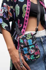 Porta celular negro con estampado de figuras de animales hechas con globos. Tiene correa larga de tela gris y cordón trenzado blanco y negro con dije metálico.