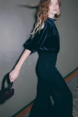 Top corto de velour negro, con cuello mao y botones forrados. Presenta canesú fruncido en la parte delantera y trasera, mangas abullonadas al codo y ribete fino en puños y bajo.