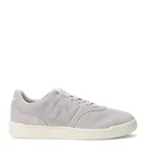 Championes urbanos New Balance de estilo retro, confeccionados en gamuza color gris claro con detalles en material sintético. Presentan el logo N característico en los laterales, cierre mediante cordones y suela de goma en tono crema.