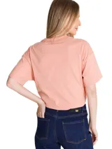 Remera de corte boxy y relajado, color rosado, con cuello redondo y mangas cortas. Presenta un estampado gráfico frontal de estilo retro con tipografía en tonos azules y rojos.