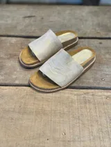 Sandalias con base marrón y tira ancha de cuero color dorado.
