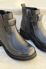 Bota corta de cuero negro con diseño de caña media, cierre lateral y detalle de tira horizontal sobre el empeine. Posee suela de goma gruesa y puntera redondeada.