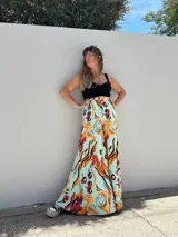 Pantalón palazzo de tiro alto con estampado abstracto en tonos naranja, rojo y negro sobre fondo celeste.