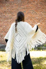 Ruana tejida en crochet de lana merino color crudo, con diseño abierto y flecos decorativos en el ruedo.