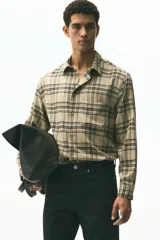 Camisa de manga larga con cuello inglés, tapeta lisa y bolsillo superior de parche. Presenta un patrón de cuadros en tonos beige claro y negro.