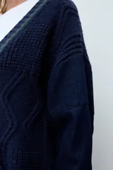 Sacón de punto con frente y espalda en tejido de ochos color azul marino, con detalles de rayas verdes en el borde. Las mangas son de tela de jean azul oscuro. Presenta cierre frontal con botones y bolsillos laterales.