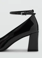 Zapato de tacón alto y ancho, color negro con acabado charol, punta cuadrada y tira ajustable con hebilla al tobillo.