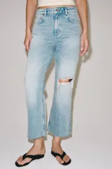 Jeans de tiro medio y corte bootcut cropped de Zara Woman Collection. Confeccionados en denim de efecto lavado en color celeste, presentan diseño de cinco bolsillos, trabillas para cinto, detalle de rotura en la rodilla izquierda y bajo evasé sin costuras. Cierre frontal con cremallera y botón metálico.
