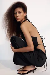 Top satinado negro de cuello halter drapeado con espalda descubierta y bajo asimétrico. Cuenta con cierre en la espalda y cuello con lazada.