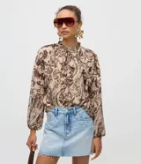 Blusa de chiffon ligera de Blue Steel con estampado paisley en tonos marrones y beige, cuello alto con lazo y volados frontales, y mangas largas con puños elásticos.