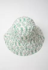 Gorro tipo bucket hat estampado con flores y hojas en tonos verde y celeste sobre fondo blanco. Es reversible.