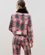 Chaqueta de denim con estampado abstracto en tonos rosados, naranjas y negros. Presenta un corte recto, cierre frontal con botones metálicos, bolsillos frontales con solapa y un cuello de piel sintética desmontable en color negro.