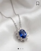 Collar de cadena fina de plata 925 con dije colgante en forma ovalada, compuesto por una piedra central de zafiro rodeada por pequeñas circonias brillantes.
