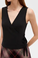 Musculosa de algodón sin mangas, de corte cruzado con cuello en V y diseño holgado, color blanco con estampado de lunares bordó y lazo lateral para ajustar.