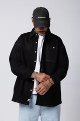 Camisa de manga larga estilo sobrecamisa, color negro, con corte oversize, cuello clásico, cierre frontal con botones y bolsillo frontal en el pecho.