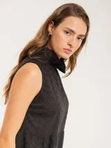 Blusa blanca sin mangas, con cuello alto con volados y detalles bordados con motivos florales.