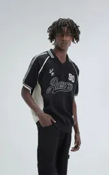 Chomba tejida de hilo color negro con punto cerrado, cuello polo con escote en V y ribetes blancos en cuello y mangas. Presenta bordados en blanco: un número "90" y la palabra "Ravers" en cursiva.