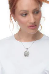 Dije plateado con detalles dorados y circonitas, con forma ovalada y diseño abstracto.