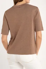 Sweater de tejido de punto fino en color arena, con cuello redondo y mangas cortas. Presenta un diseño minimalista con un pequeño detalle metálico en el ruedo.