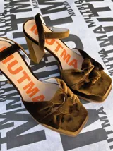 Sandalias de tacón alto Mutma modelo Ñoma, confeccionadas completamente en terciopelo color verde militar. Presentan una plataforma delantera, detalle de doble nudo o moña en la puntera, taco ancho y tira con hebilla ajustable en el tobillo.