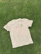 Remera color arena de manga corta con estampa en la espalda de un jarrón con flores.