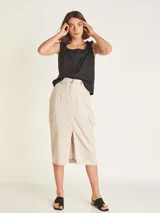 Falda midi color beige, de tiro alto con elástico en la cintura trasera, cierre y botón delantero. Tiene bolsillos delanteros y bolsillos cargo a los costados, con tajo en el delantero.