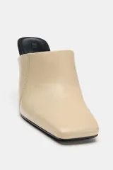 Zapato de tacón tipo mule en piel, de color beige con tacón fino y plantilla en contraste de color negro. Presenta escote redondo, costuras pespunteadas en los laterales y acabado en punta cuadrada.