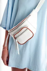 Riñonera blanca con textura tipo piel de cocodrilo, cierre superior y bolsillo frontal con cierre, ambos con ribete marrón.