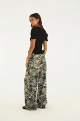 Pantalón de tiro medio de denim con estampado floral multicolor en tonos verdes, azules y naranjas, de corte wide leg y piernas amplias.