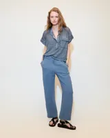 Remera blanca de lino con cuello mao, media cartera con broches metálicos y manga japonesa. Presenta un bolsillo frontal tipo plaqué, recortes laterales en sisa con detalles de encaje y ruedo redondeado con corte escalonado.