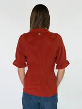 Top de tejido de punto color terracota, con escote en V, cuello camisero y cartera frontal con botones. Presenta mangas cortas con textura calada y puños con volados.