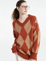 Sweater de punto con escote en V y diseño de rombos en tonos marrón y naranja. Presenta un corte holgado, mangas largas con puños acanalados y terminación de ruedo también acanalada.