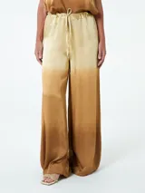 Pantalón palazzo color beige con efecto degradado hacia el marrón. Tiene cintura alta con elástico y cordón ajustable.