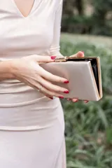 Clutch de mano color arena con textura de rayas verticales y cierre dorado con aplique de strass.