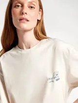 Camiseta de corte oversized color beige, con cuello redondo y estampa pequeña en el pecho con diseño tipo sello postal.