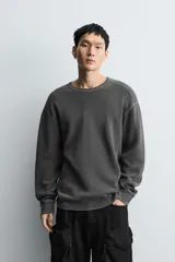 Camiseta de manga larga con cuello redondo, confeccionada en tejido de algodón con textura tipo waffle y efecto lavado. Presenta un corte relajado con puños en rib y bajo irregular.