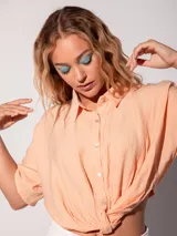 Camisa de manga corta color salmón, con textura arrugada, cuello camisero y botones nacarados. Se anuda en la cintura al frente y tiene elástico en la espalda.