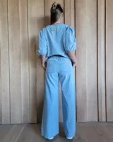 Pantalón de denim estilo palazzo, color azul claro, con cintura elástica en la parte posterior, bolsillos frontales y costuras verticales decorativas a lo largo de las piernas.