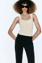 Body de tejido elástico color beige, sin mangas y con diseño de escote cuadrado. Cuenta con cierre en la parte inferior con botones a presión.