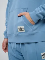 Canguro con capucha Umbro modelo RLXD, color celeste, con bolsillos tipo canguro y parche con logo de la marca bordado en el frente.