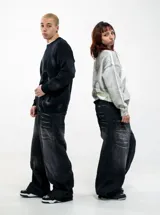 Pantalón de jean estilo baggy fit, color negro con efecto lavado y detalles de roturas horizontales en la parte frontal. Presenta un corte holgado y tiro bajo.
